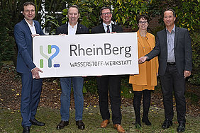 Fünf Personen, unter anderem Frank Herhaus, Stephan Sanelmann, Jochen Hagt und Elke Reichert, halten ein Schild mit dem Logo der H2-Werkstatt hoch. Text: RheinBerg Wasserstoff-Werkstatt