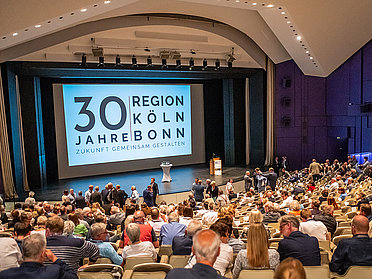 Gäste des Langen Tages im Grpßen Saal des Forum Leverkusen. Auf der Leinwand das Jubiläumslogo des Region Köln/Bonn e.V.
