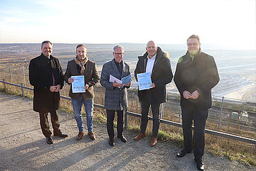 Bodo Middeldorf, Andreas Heller, Jürgen Steinmetz, Frank Rock und Dr. Tim Grüttemeier halten das Positionspapier in die Kamera. Im Hintergrund ist ein Tagebau zu sehen.